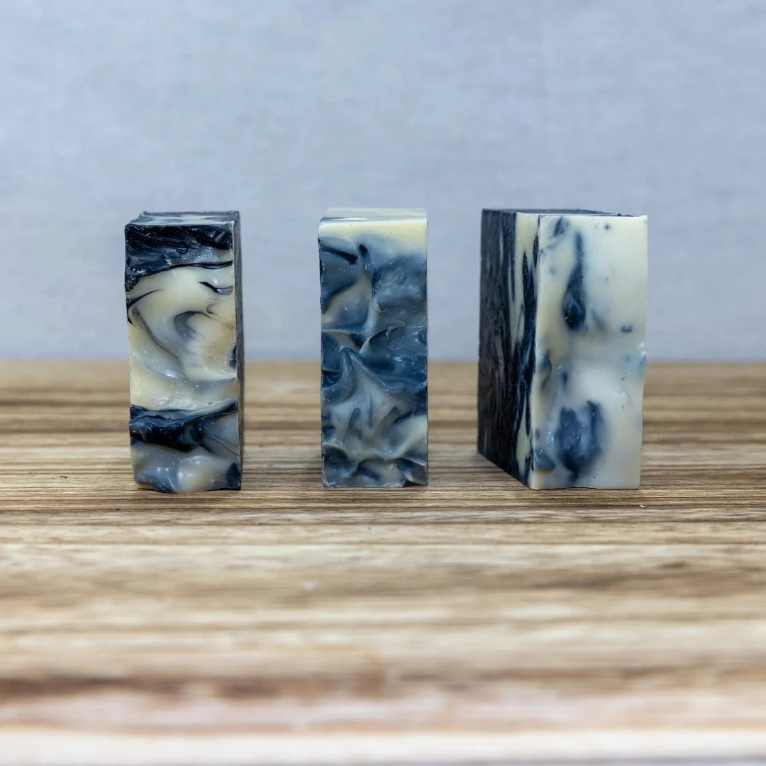 Three indigo blue color rectangular bars of soap with marble like patterns on a wooden surface.